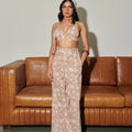 Woman in a floral hand block printed pants and bralette outfit standing in front of a brown leather couch. 