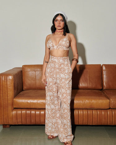 Woman in a floral hand block printed pants and bralette outfit standing in front of a brown leather couch. 